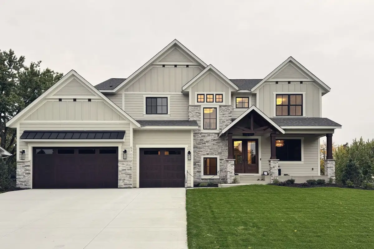 The Craft Homes model in Edina: a two-storey home of cream board-and-batten and stone with a timber-framed porch and three garage doors