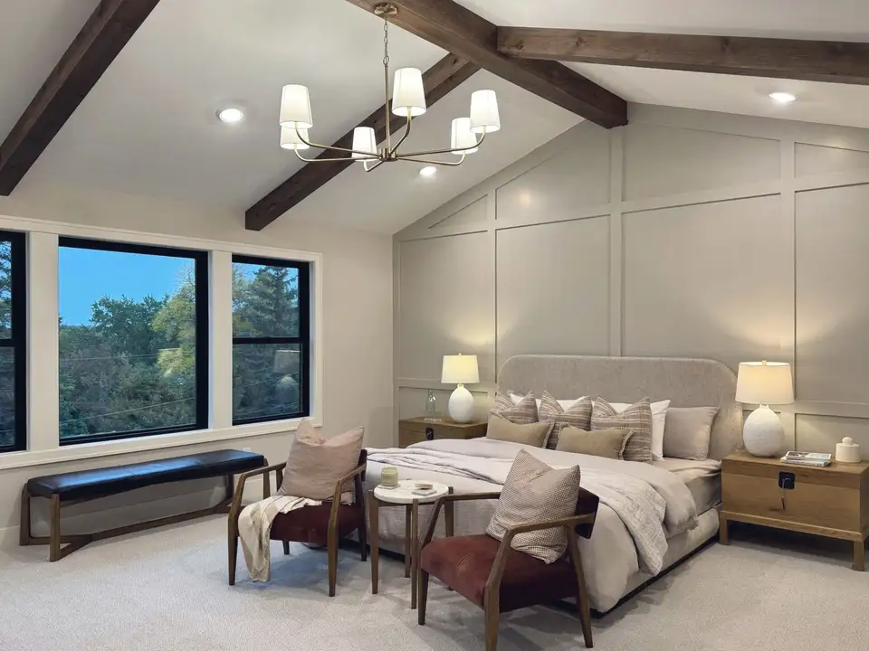 A primary bedroom under a vaulted beamed ceiling, with a panelled wall behind the bed