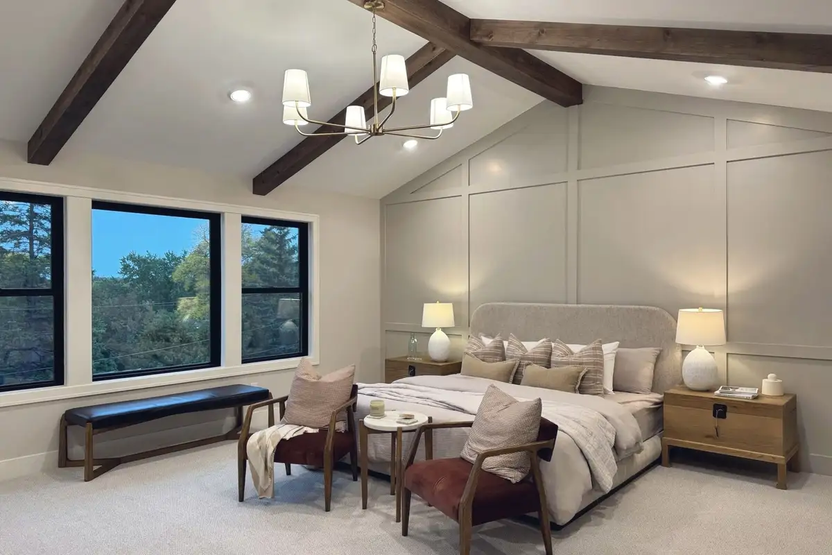 A primary bedroom under a vaulted beamed ceiling, with a panelled wall behind the bed, in the Craft Homes model in Edina