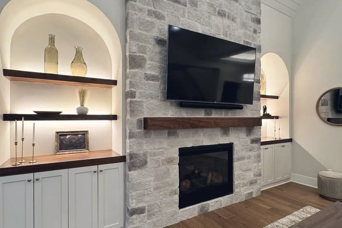 A stacked-stone fireplace between lit arched niches with walnut shelves, in the TJB Homes model in Edina