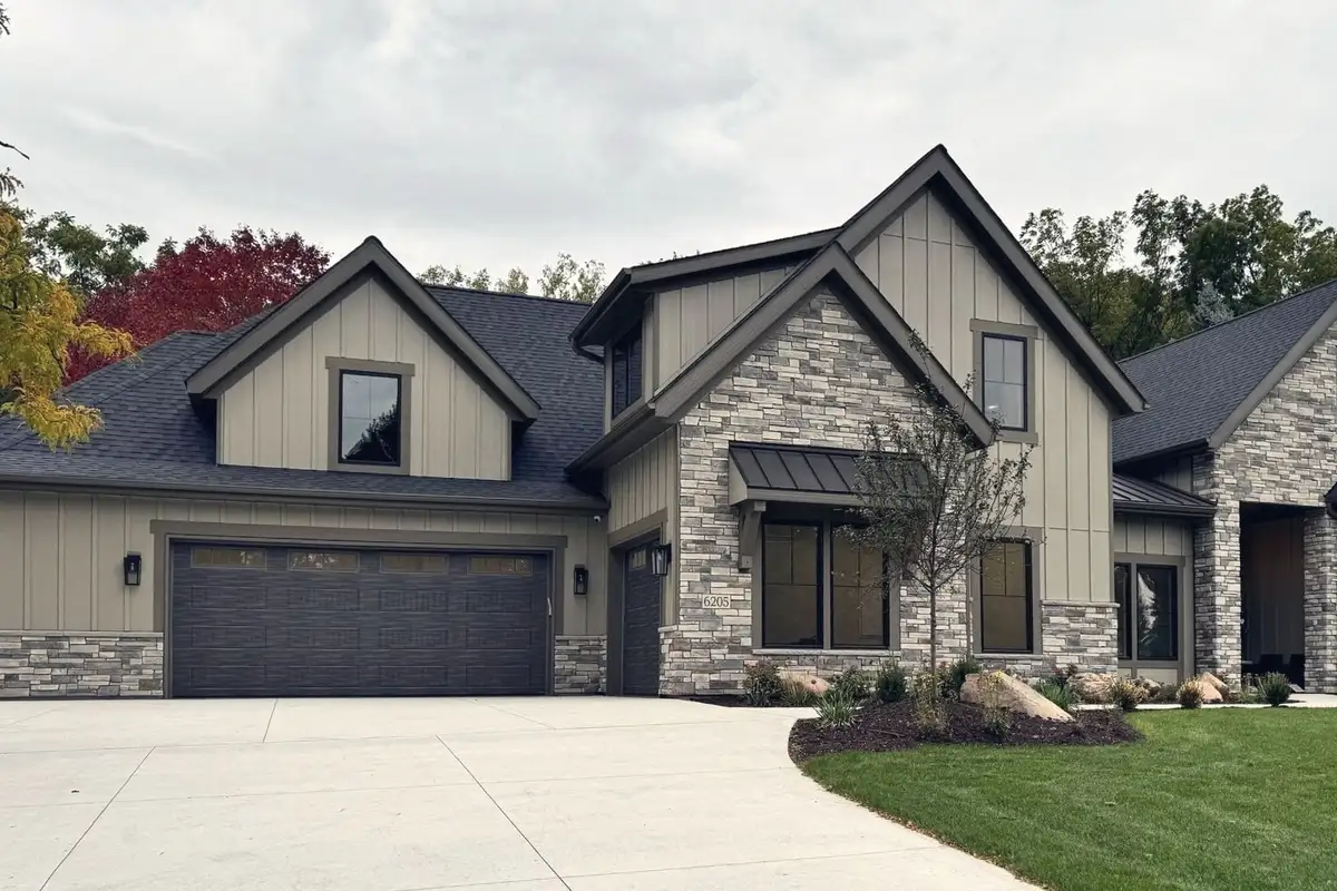 A TJB Homes model in Edina: a new home of stacked stone and sage board-and-batten under steep gables, beside a wide garage