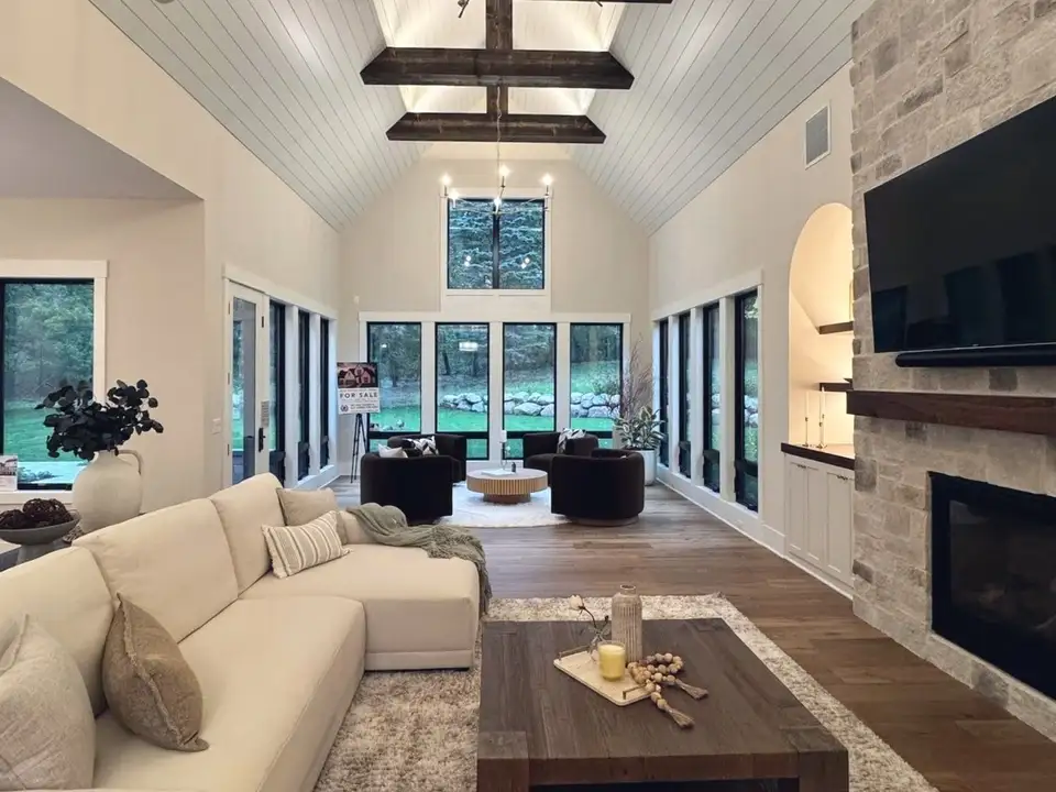 A vaulted great room with dark timber beams, a stacked-stone fireplace and a wall of windows