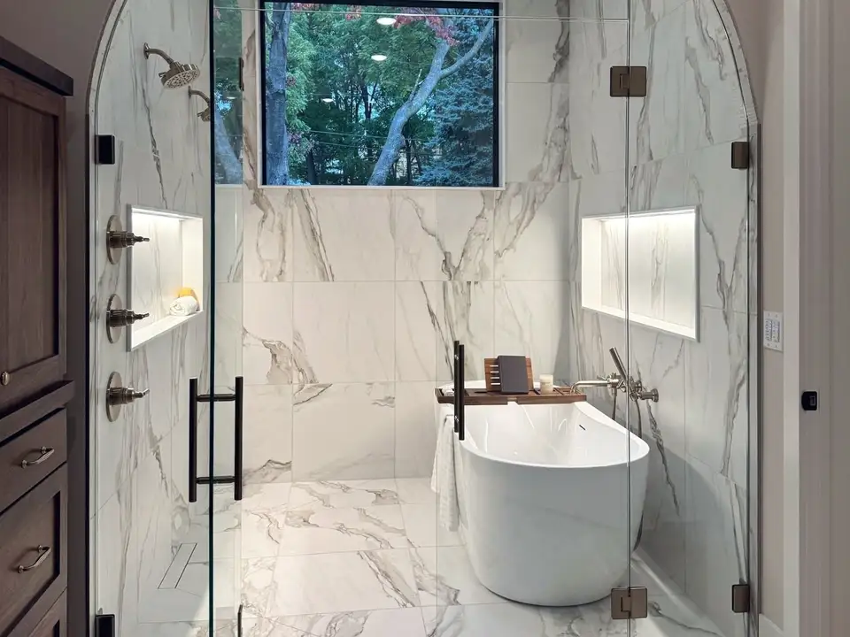 A primary bath with an arched glass wet room in marble-look tile around a freestanding tub