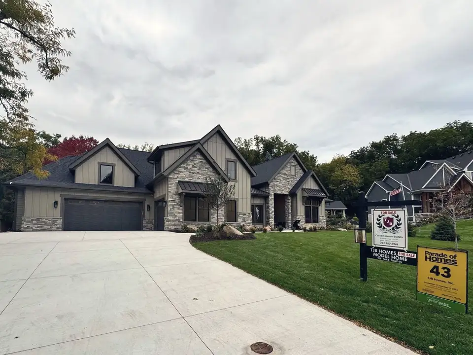 A new stone and board-and-batten home seen from the street, with its builder sign and the Parade of Homes entry 43 sign on the lawn