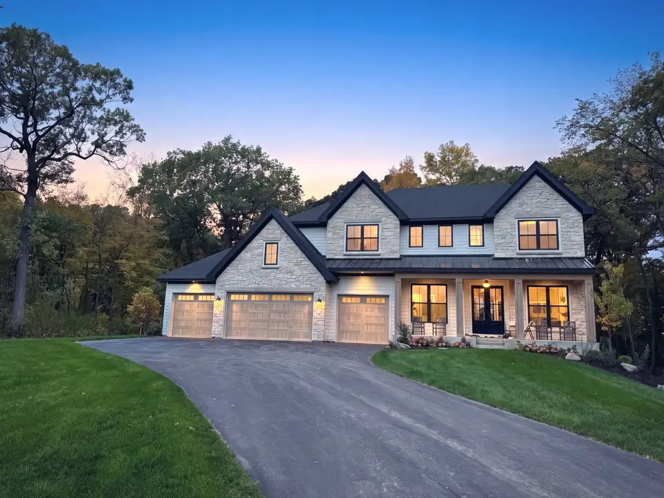 A two-storey stone home at dusk, its windows lit, above a curving drive