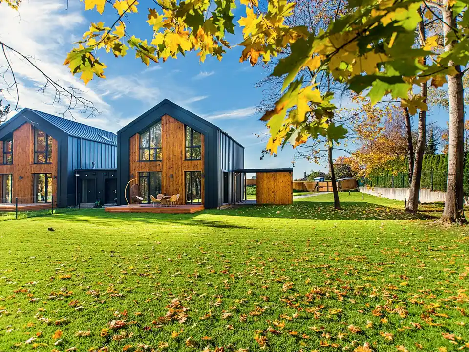 Barn-style gabled homes in dark timber, across a lawn in autumn