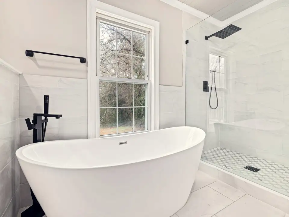 A freestanding tub under a window, beside a glass shower