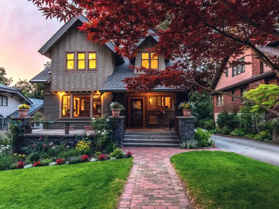A craftsman home at dusk under a red maple, its windows lit