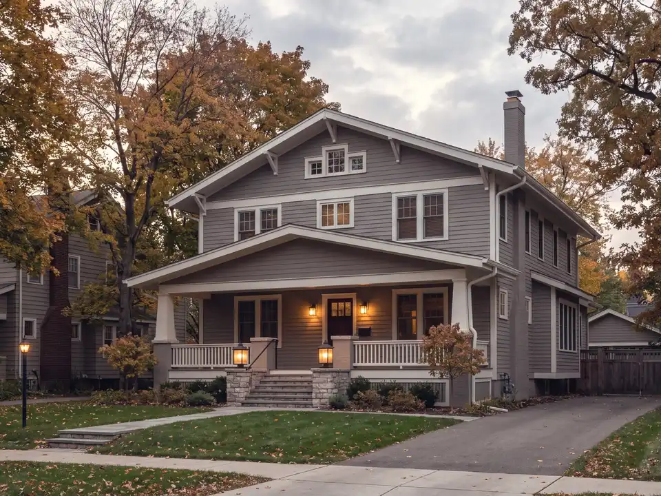 A painted craftsman home with a wide lit porch on an autumn street