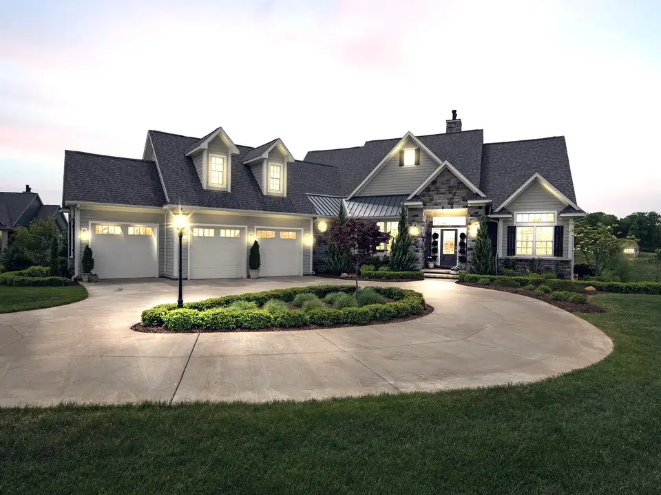 A large custom home at dusk, its windows lit, with a circular drive