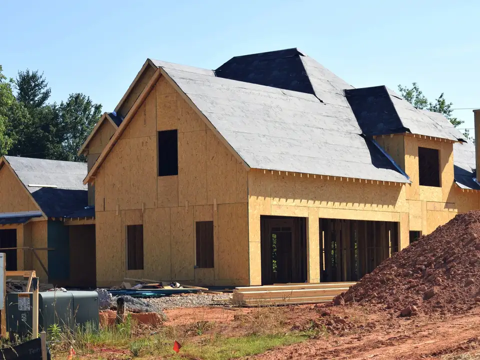 A two-storey house under construction, sheathed and roofed, among trees
