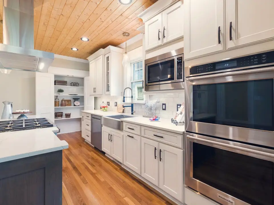 A renovated white kitchen under a wood-plank ceiling