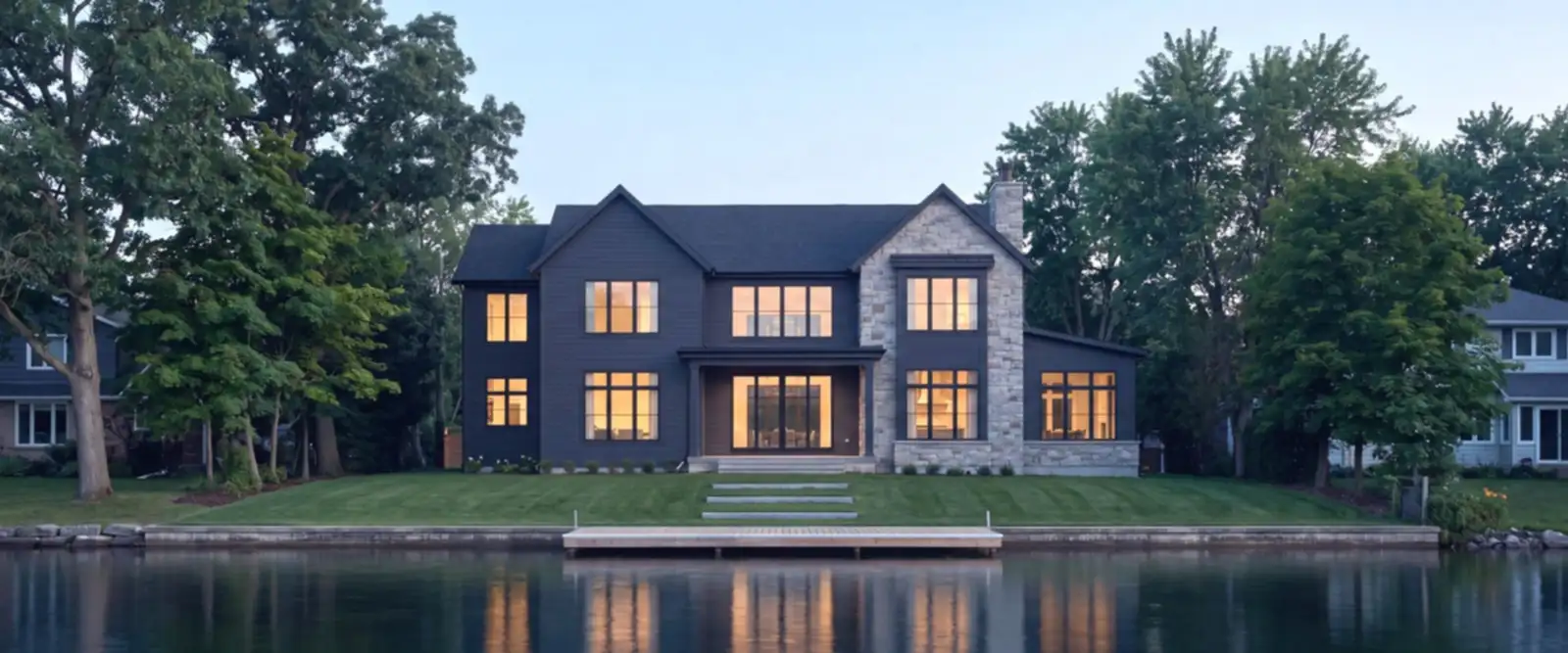 A contemporary lake home seen across calm water at blue hour, one dock, oaks and maples