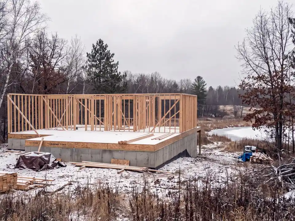 A house being framed on its foundation in light snow