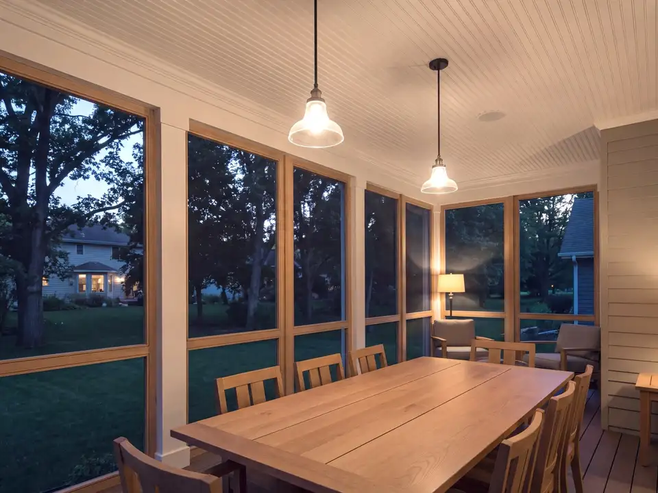 A screened porch with a dining table, looking onto oaks and a lawn at dusk