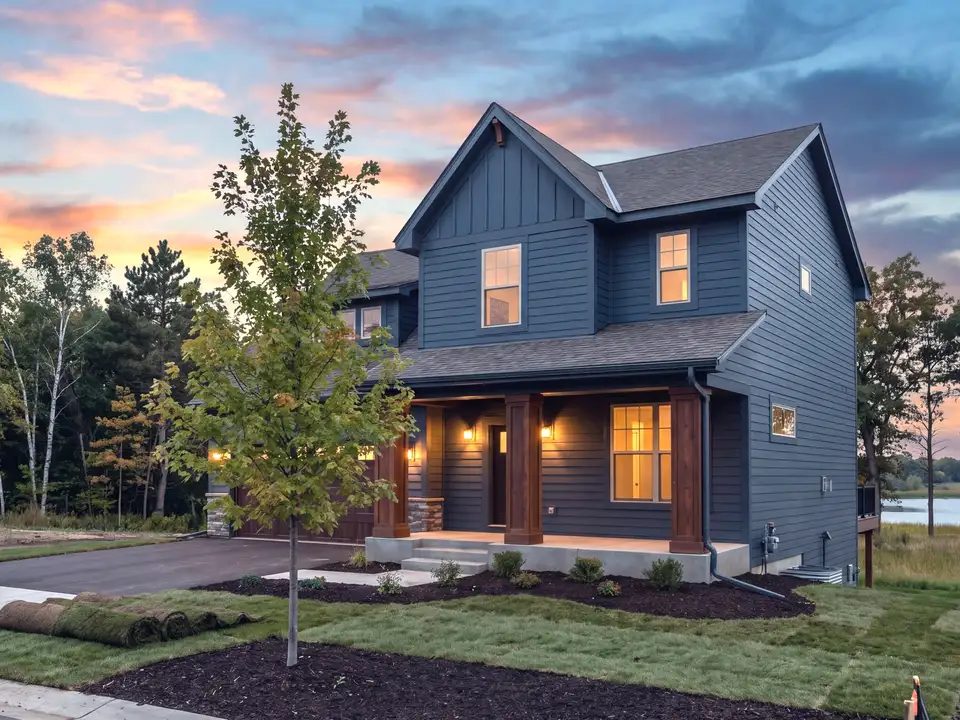 A new two-storey home with a deep front porch on a new street at sunset