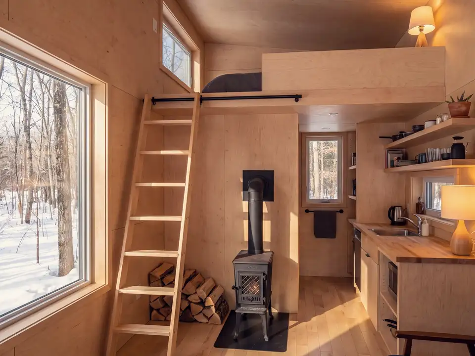 A birch-panelled tiny house with a loft ladder and a wood stove
