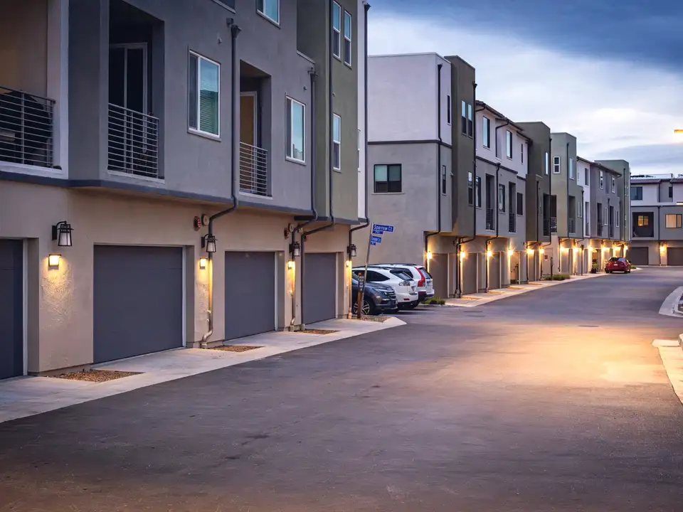 A row of townhomes at dusk, their garage lights on